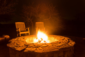 Fire pit aflame with two empty chairs and dark forest - obrazy, fototapety, plakaty