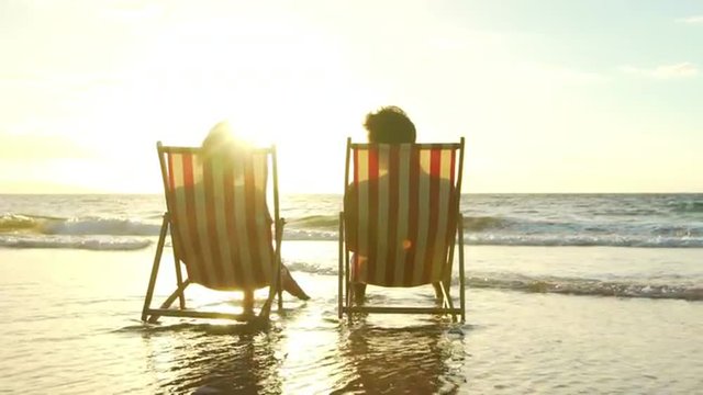 Relaxing Couple on Tropical Resort Luxury Vacation. Beach Chairs in the Sunset. Slow Motion.