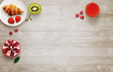 Fruit breakfast with free space on wooden table. Croissant, pomegranate, raspberries, juice, kiwi, strawberries with top view.