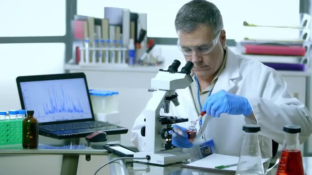 A microscope and computer being used by this scientist in his laboratory to analyze a sample.