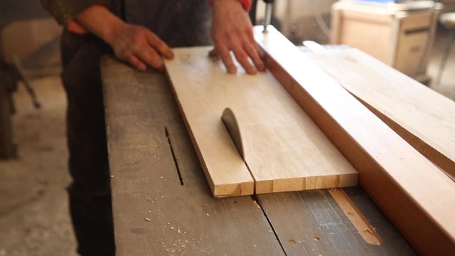 Carpenter sawing plank on a saw circulation in worksho