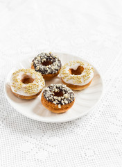 Mini donuts with lemon and chocolate icing on a white plate on bright tablecloths. Vintage style