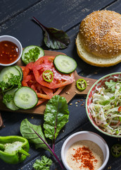delicious veggie Burger. Raw ingredients - cabbage, tomato, cucumber, lettuce, pepper, sauce vegetarian and a homemade bun for burgers, on a dark wooden surface