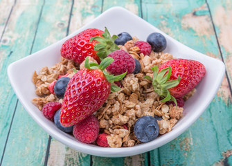 Breakfast cereal with strawberries, blueberries, raspberry fruits in white bowl over wooden background