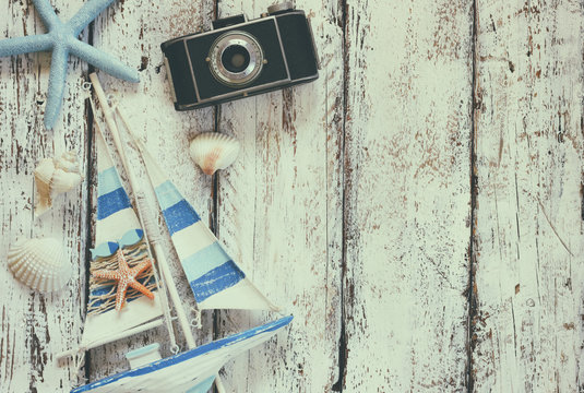 top view image of photo camera, wood boat, sea shells and star fish over wooden table
