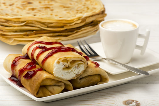 Pancakes filled with cottage cheese and cup of coffee on the wooden background.