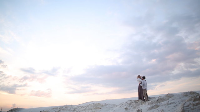 man and woman are kissing on sand quarry at sunset