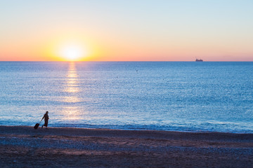 Fototapeta premium Exotic Vacation Silhouette of Female pulling Travel Suitcase along Ocean Beach
