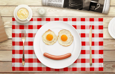 Breakfast smiling face. Eggs, hot dog, plate, tablecloth, coffee, newspaper on table with a top view. 