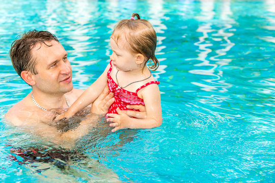 Active father teaching his toddler daughter to swim in pool on tropical resort. Summer vacations and sport  concept
