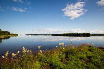 A beautiful summer day in northern Sweden. A lake with calm water, blue skies and green grass. 