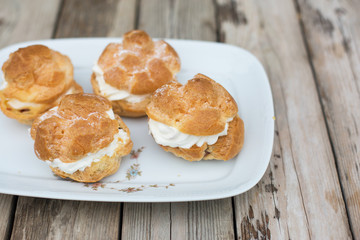 four big homemade profiteroles with cream on wooden table - perfect summer desert