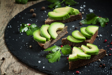 Sandwich with avocado, black rye bread and spices on dark stone