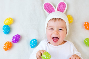 Baby boy in bunny hat lying on green blanket with easter eggs