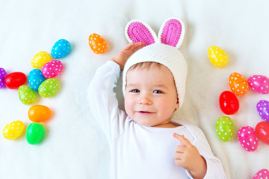 Baby boy in bunny hat lying on green blanket with easter eggs