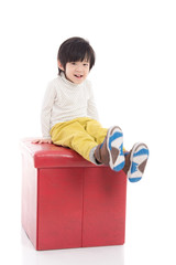 Cute asian boy sitting on red stool isolated