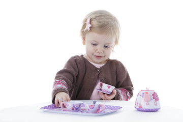 toddler girl playing with tea set, holding tea cup, isolated on white background