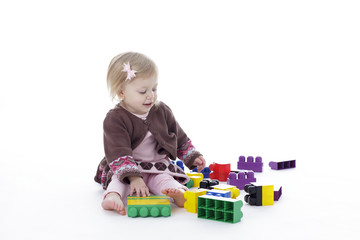 toddler girl playing with colored building blocks, isolated on white background