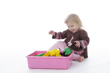 toddler girl picking up toys in pink bin, isolated on white background
