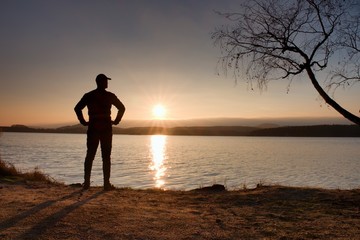 Lone sportsman looking at colorful  sunset on shore of autumn lake