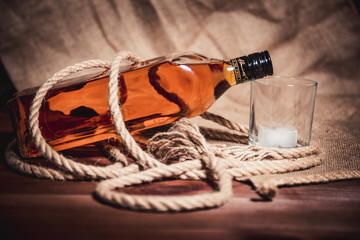 Whisky glass with ice, a bottle of whiskey and a rope