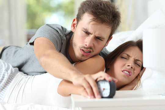 Angry couple turning off the alarm clock