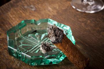 cigar with ashtray and alcohol drink in background