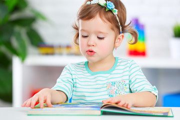 cute baby girl reading book at home
