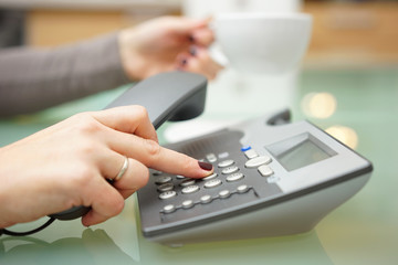 Woman is pressing button on on the phone dial pad and drinking c