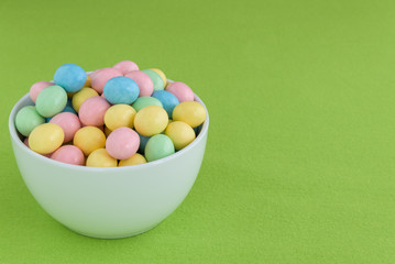 Pastel candy coated Easter eggs in a smooth round while bowl on a spring green background
