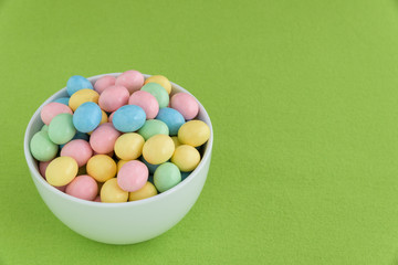 Pastel candy coated Easter eggs in a smooth round while bowl on a spring green background
