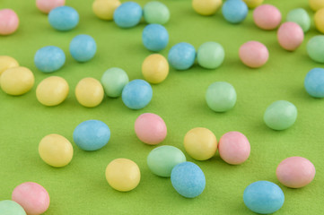 Pastel candy coated Easter eggs spilled out on a spring green background

