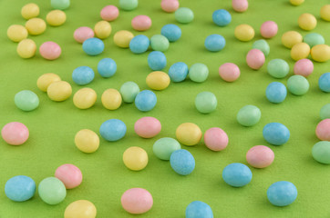 Pastel candy coated Easter eggs spilled out on a spring green background
