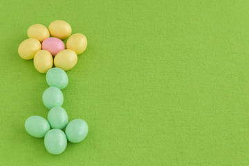 Pastel candy coated Easter eggs arranged as a flower with stem on a spring green background
