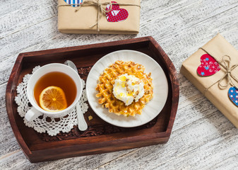 Lemon tea, waffles with ice cream, honey and nuts in a vintage tray, homemade Valentine's day gifts in kraft paper on a wooden table