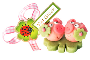 Two marzipan pigs with cloverleaf and good luck (in German) written on a background