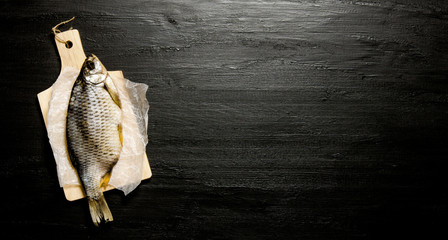 Dried fish on wooden board. On black chalkboard. Free space for text.