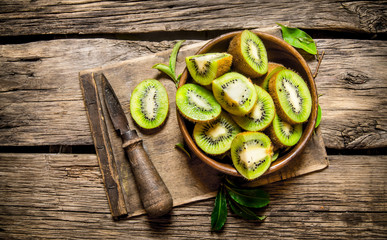 sliced kiwi fruit in a wooden cup with a knife.
