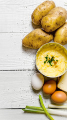 Cooking mashed potatoes ingredients: potatoes, milk, eggs, butter and other on a white wooden table.