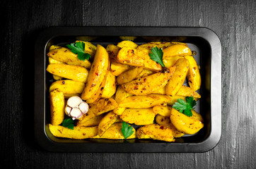 Baked potatoes with spices and salt on black wooden table.