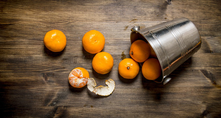 Fallen bucket with fresh tangerines. On wooden table.