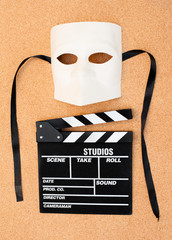 White mask and movie clapper on cork wooden background