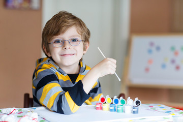 Little kid boy drawing with colorful watercolors indoors