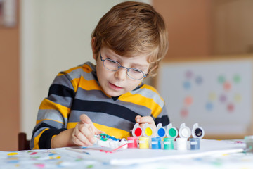 Little kid boy drawing with colorful watercolors indoors