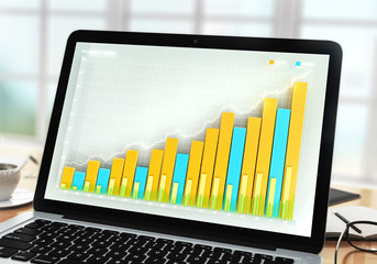 Business graph on laptop screen on office table at sunrise