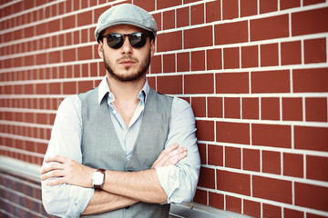 casual young man stands with his back against a brick wall