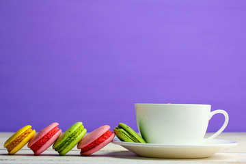 Colorful delicious macaroons on a plate with a Cup of coffee on wooden table on purple background