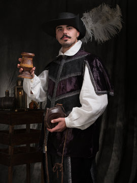 A man in period costume and hat raises a glass of wine