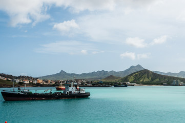 Ship in front of small town at the blue ocean coast with cloudy mountain background, Cape Verde island