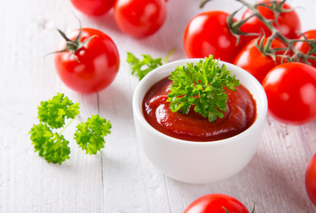 Bowl of tomato sauce and cherry tomatoes on wooden table.